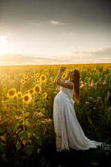 Beautiful caucasian pregnant woman walking in the summer at sunset in a field of blooming sunflower