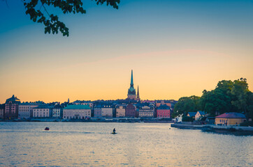 Watercolor drawing of historical town quarter Gamla Stan with traditional typical buildings with colorful walls, Skeppsholmen island park and boat on Lake Malaren water at sunset, Stockholm, Sweden