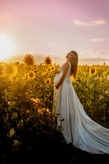 Beautiful caucasian pregnant woman walking in the summer at sunset in a field of blooming sunflower