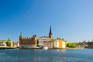 Fototapeta premium Watercolor drawing of Riddarholmen island district with Riddarholm Church spires and typical sweden colorful gothic buildings, boat ship moored on Lake Malaren water from Kungsholmen, Stockholm