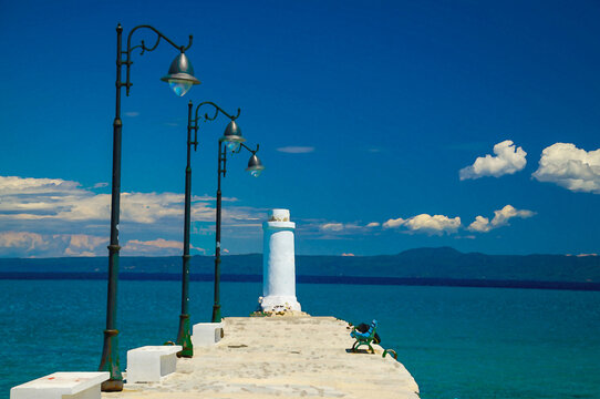 Watercolor drawing of White pier jetty with bench, lampposts lighthouse on blue paradise water of Toroneos kolpos gulf, blue sky white clouds over Sithonia peninsula in Pefkohori, Halkidiki, Greece