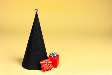 Black minimalistic Christmas tree in the form of a cone with red gifts on a yellow background. pop-art style