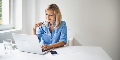 young and blond business woman with blue shirt and glasses is working in office and is happy