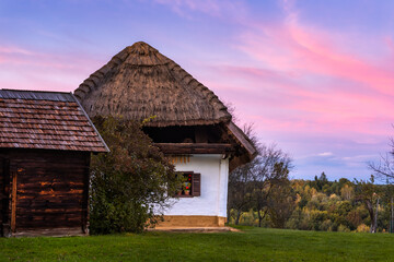 Fototapeta na wymiar Purple twilight over a traditional straw-roofed house in the open-air museum of Szalafő, Hungary