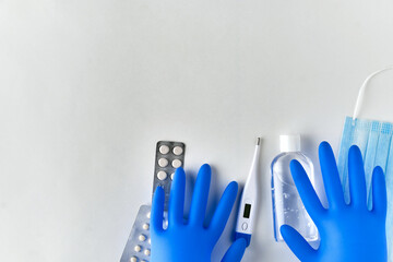 two hands in blue gloves lie on blisters with pills, a blue mask, a white thermometer and an antiseptic in a transparent plastic bottle on a light background