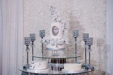 Table with a wedding cake, candles and flowers. Photo-wall, wedding decoration space or place from white and silver style.