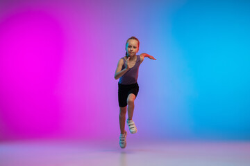 Fototapeta na wymiar Playful. Teenage girl, professional runner, jogger in action, motion isolated on gradient pink-blue background in neon light. Concept of sport, movement, energy and dynamic, healthy lifestyle.