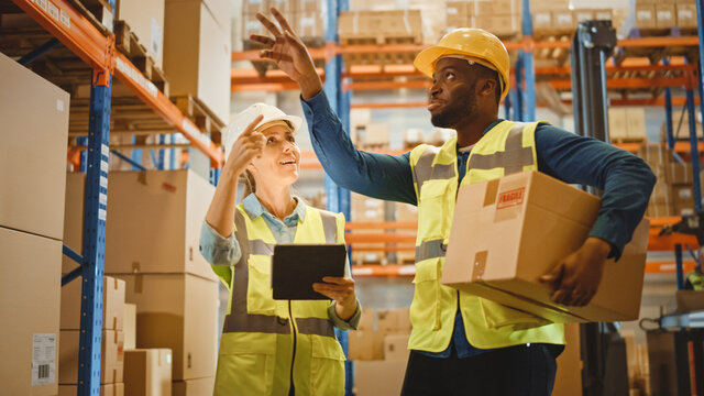 Retail Warehouse full of Shelves with Goods in Cardboard Boxes, Male and Female Supervisors Use Digital Tablet and Look For a Right Shelf. Forklift Working in Logistics Storehouse