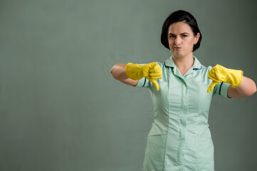 Young cleaning woman wearing a green shirt and yellow gloves showing double dislike