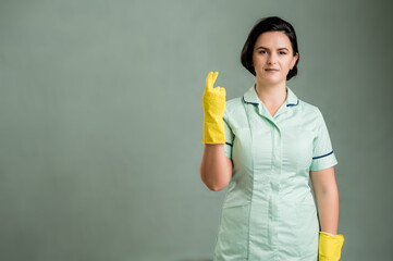 Young cleaning woman wearing a green shirt and yellow gloves showing good luck