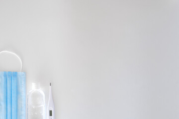 antiseptic in a transparent plastic bottle with a white cap white and white electronic thermometer lie on a light background next to a blue mask