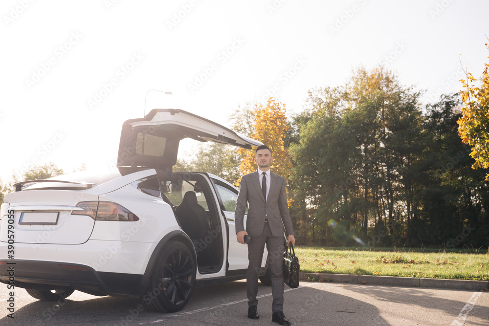 Wall mural businessman gets out of a white executive car at car park during day time. the business person is ca