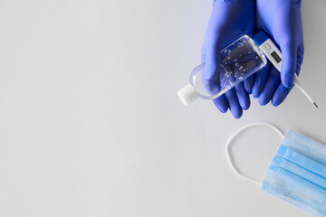 female hands in blue gloves hold an antiseptic and a thermometer, blue mask, on a light background