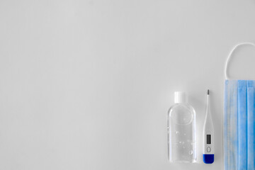 antiseptic in a transparent plastic bottle with a white cap white and white electronic thermometer lie on a light background next to a blue mask