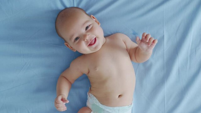 A nice little caucasian newborn baby is funny smiling, lying at the back. Portrait of a playful and energetic child close-up.