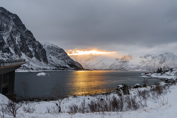 Scenic view over morning sun breaking through dense clouds behind snow-clad mountains near lake on...