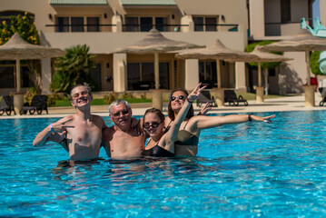 Cheerful happy father or grandfather and children laughing and hugging in swimming pool. Enjoying pool party with friends. Happy family relaxing in swimming pool