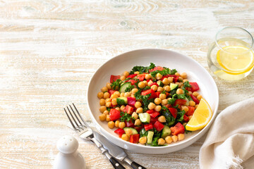 Healthy vegan salad with chickpeas, tomatoes, cucumbers, bell peppers and kale on light wooden background, space	