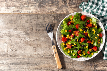 Mexican salad with black beans, corn,tomatoes,lettuce and pepper on wooden table.Top view. Copy space