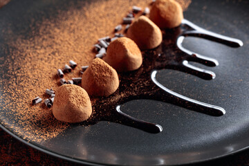 Chocolate truffles on a black plate with chocolate sauce.