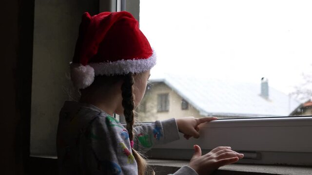 Little girl by the window in Santa hat. Orphans and Christmas . Orphanage life and holidays.