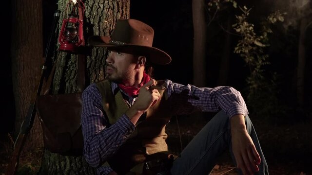 Cowboy with a cigar in the forest at night. Life in the wild west of America. 4K