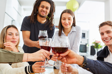 Glückliche Gruppe Freunde stößt zusammen mit Glas Rotwein in Küche an