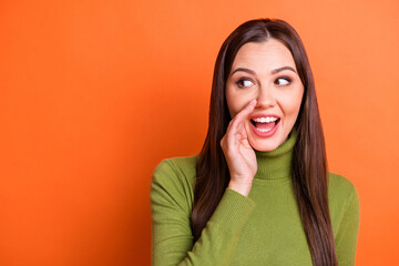 Portrait of optimistic cute brunette hairdo girl hand face look empty space wear green sweater isolated on pumpkin color background