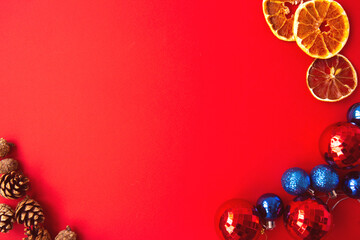 Multicolored red and blue Christmas balls and spruce cones, dried orange wedges on bright red background. Christmas decorations. Concept of celebrating new year