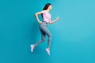 Fototapeta na wymiar Full length profile photo of sportive cute girl jump run look empty space wear pink t-shirt sneakers jeans isolated blue color background