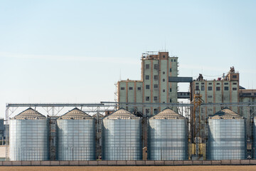 silver silos on agro manufacturing plant for processing drying cleaning and storage of agricultural products, flour, cereals and grain. Large iron barrels of grain. Granary elevator