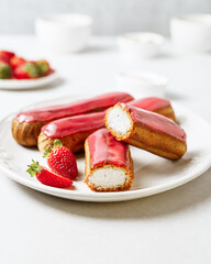 Glazed eclairs with cream filling served with strawberries