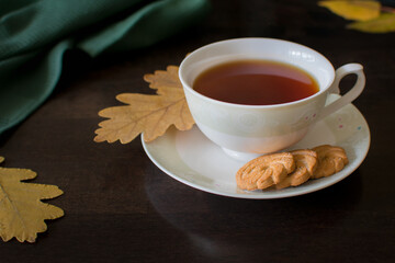 Black tea with cookies on a dark background with yellow oak leaves. view from above. The photo is taken with selective focus and has a noise effect.