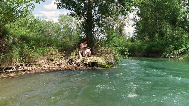 Joven adolescente leyendo en el borde de un arroyo y dron volando sobre el agua