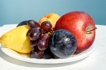 Fresh fruit on a white plate against a blue wall, healthy food concept