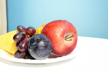 Fresh fruit on a white plate against a blue wall, healthy food concept