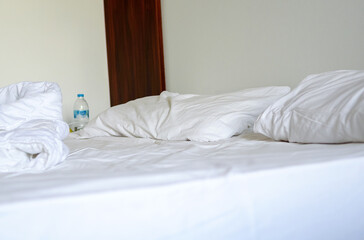 Close-up of white bedding sheets and pillow against the background of a hotel room, unmade bed