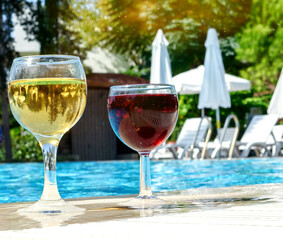 Two glasses of red and white wine are placed by the pool. The concept of a pleasant stay.