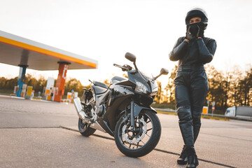 Brutal biker near motorcycle on the background of a gas station - obrazy, fototapety, plakaty
