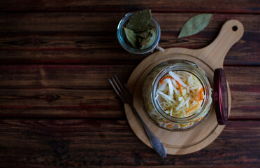 An open jar of sauerkraut on a brown wooden table. Image with copy space, horizontal orientation, top view.