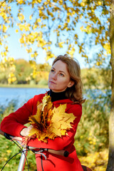 Portrait of a happy girl in red, with a bouquet of autumn leaves on the background of the lake. Outdoor.