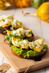 Toasted sandwiches with brie cheese, baked pumpkin and salad, arugula and mozzarella, delicious vegetable snacks on a wooden board