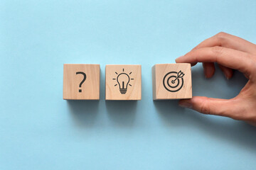 Wooden blocks with drawings of the question, light bulbs and a target on them. Symbol of the question, idea origin, and start of action