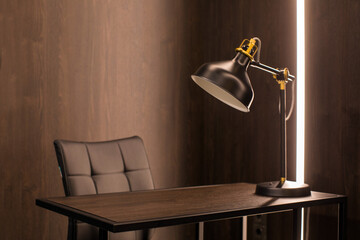 Comfortable chair placed near desk with lamp in corner of illuminated modern workplace