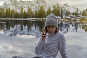 A woman talking on the phone and in the background a lake and the mountain.