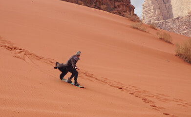 Young man sand dune surfing wearing bisht - traditional Bedouin coat. Sandsurfing is one of the...