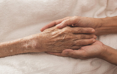 A woman holding a hand An old woman lying in bed sick.