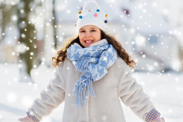 Fototapeta na wymiar childhood, leisure and season concept - portrait of happy little girl in winter clothes outdoors at park over snow