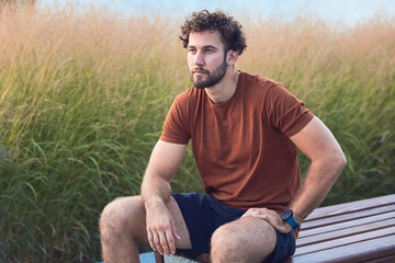 Young sporty man making pause on a bench after exercising in urban environment.
