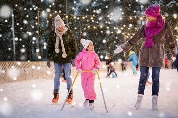 christmas, family and leisure concept - happy mother, father and daughter with support frame at outdoor skating rink in winter over snow